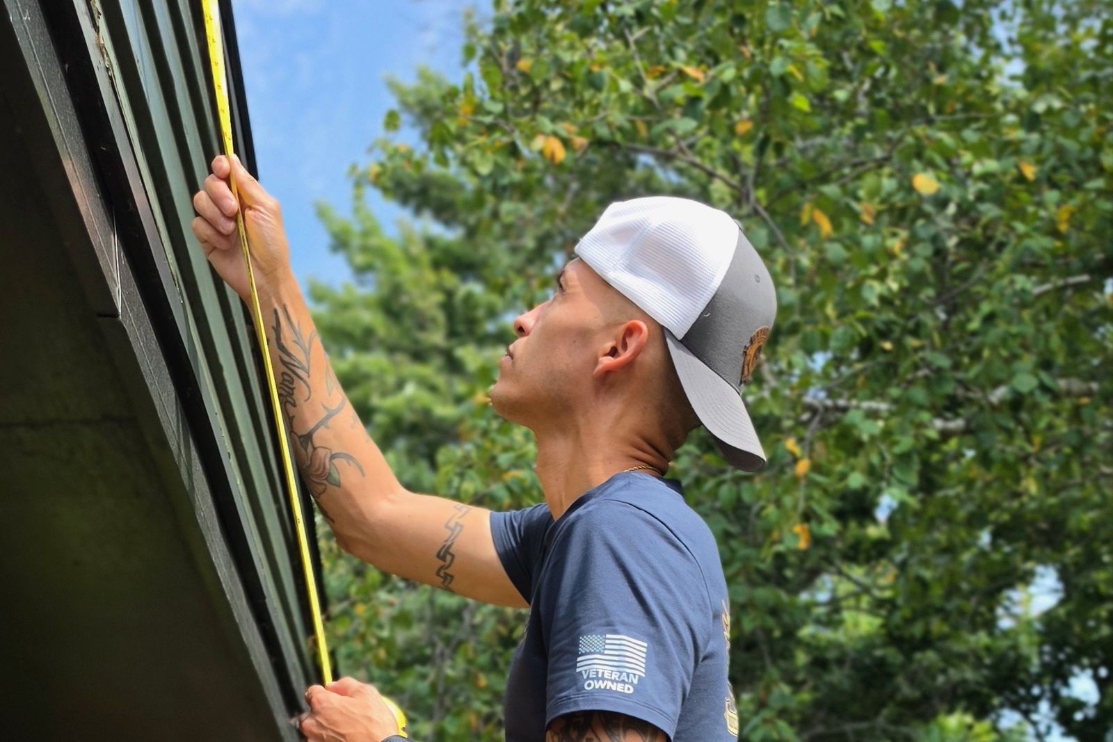 Sammy Bryson on a ladder, measuring a fascia board with a tape measure